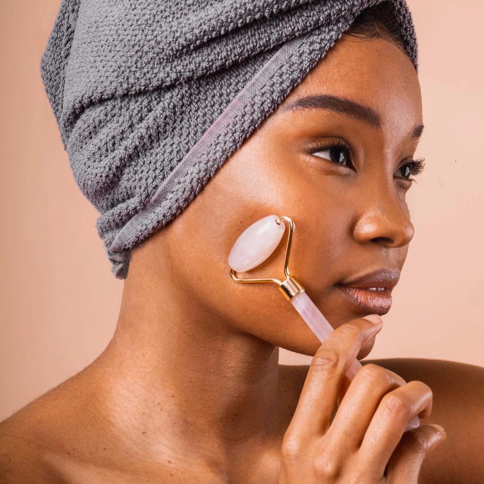 Woman with a towel on her head uses a quartz facial roller.