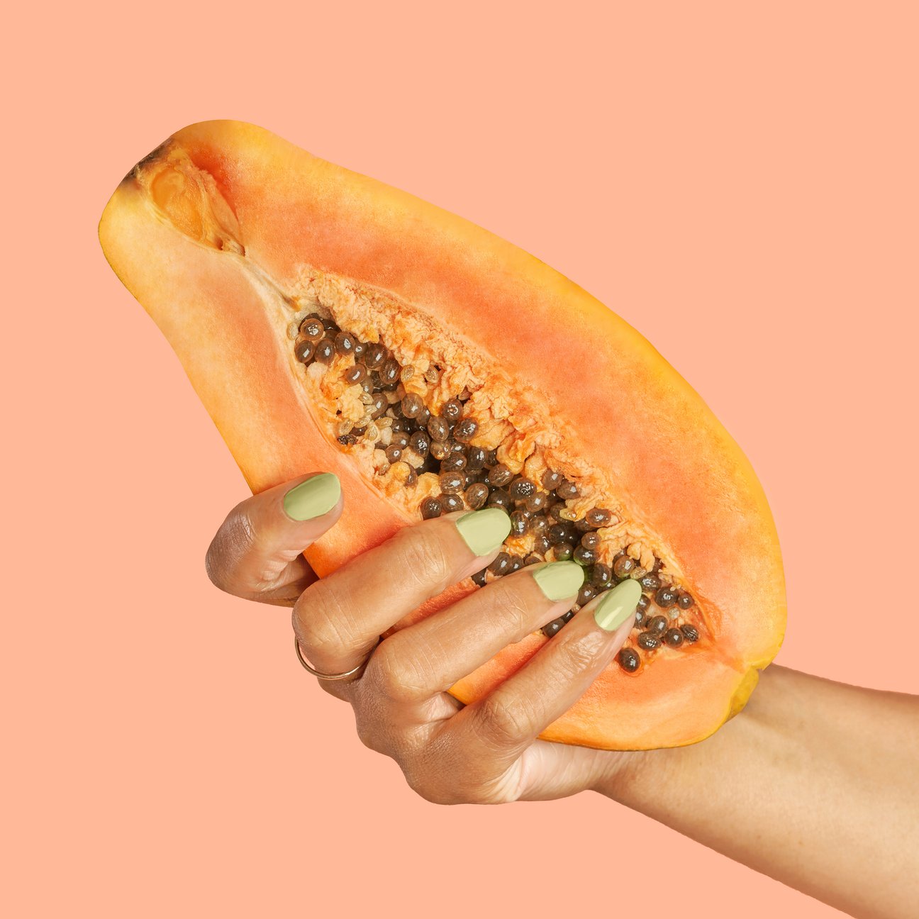 Woman's hand with colourful nails holding a papaya